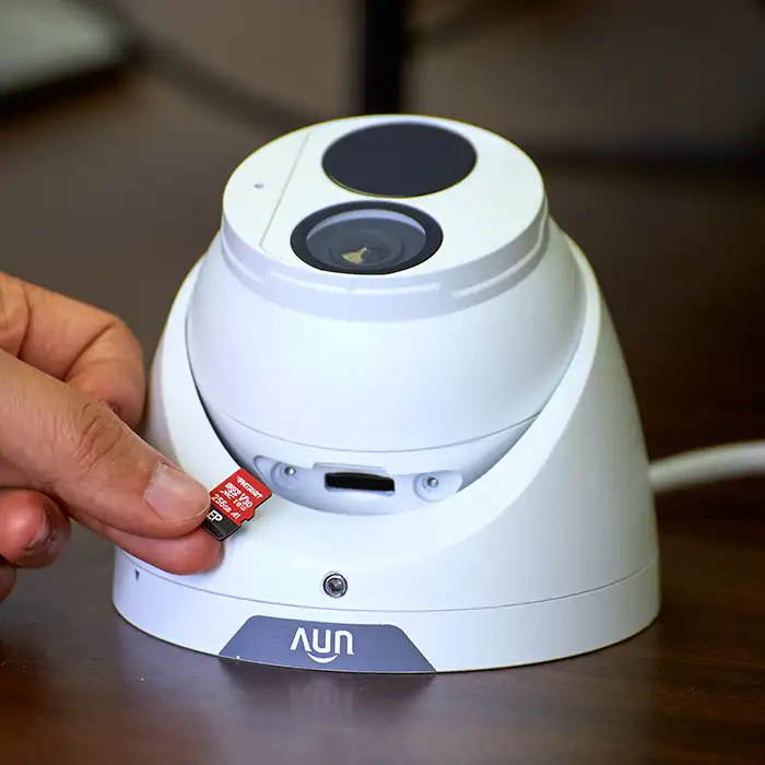 A hand inserting a MicroSD card into a security camera