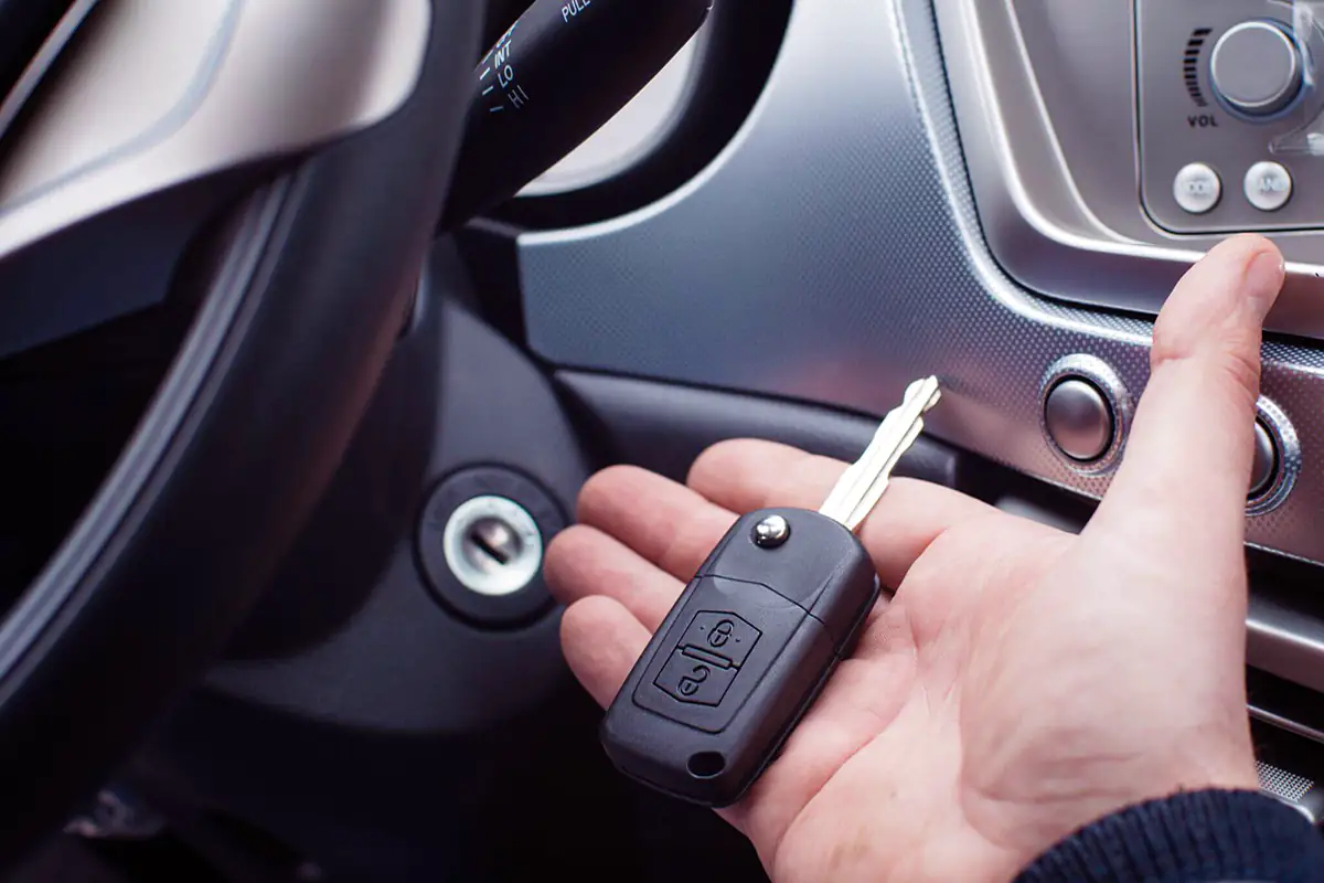 Man holding a car key near the steering wheel of a vehicle