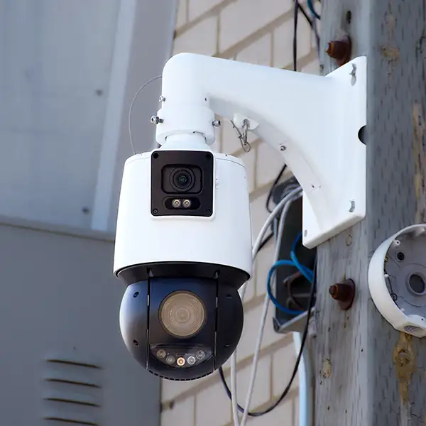 A PTZ camera mounted on a wooden post on the side of a building