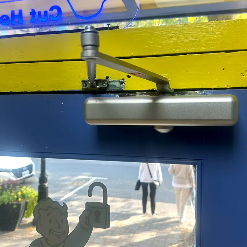 An automatic door closer installed on a blue door at a locksmithing shop