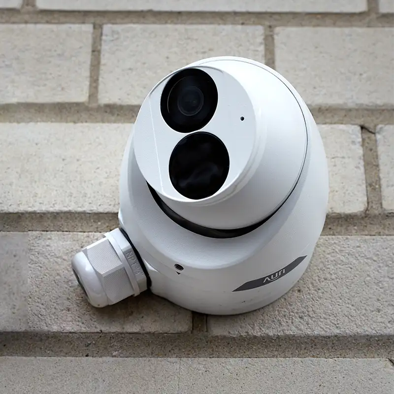 A white security camera with the UNV logo mounted on a light coloured brick wall.